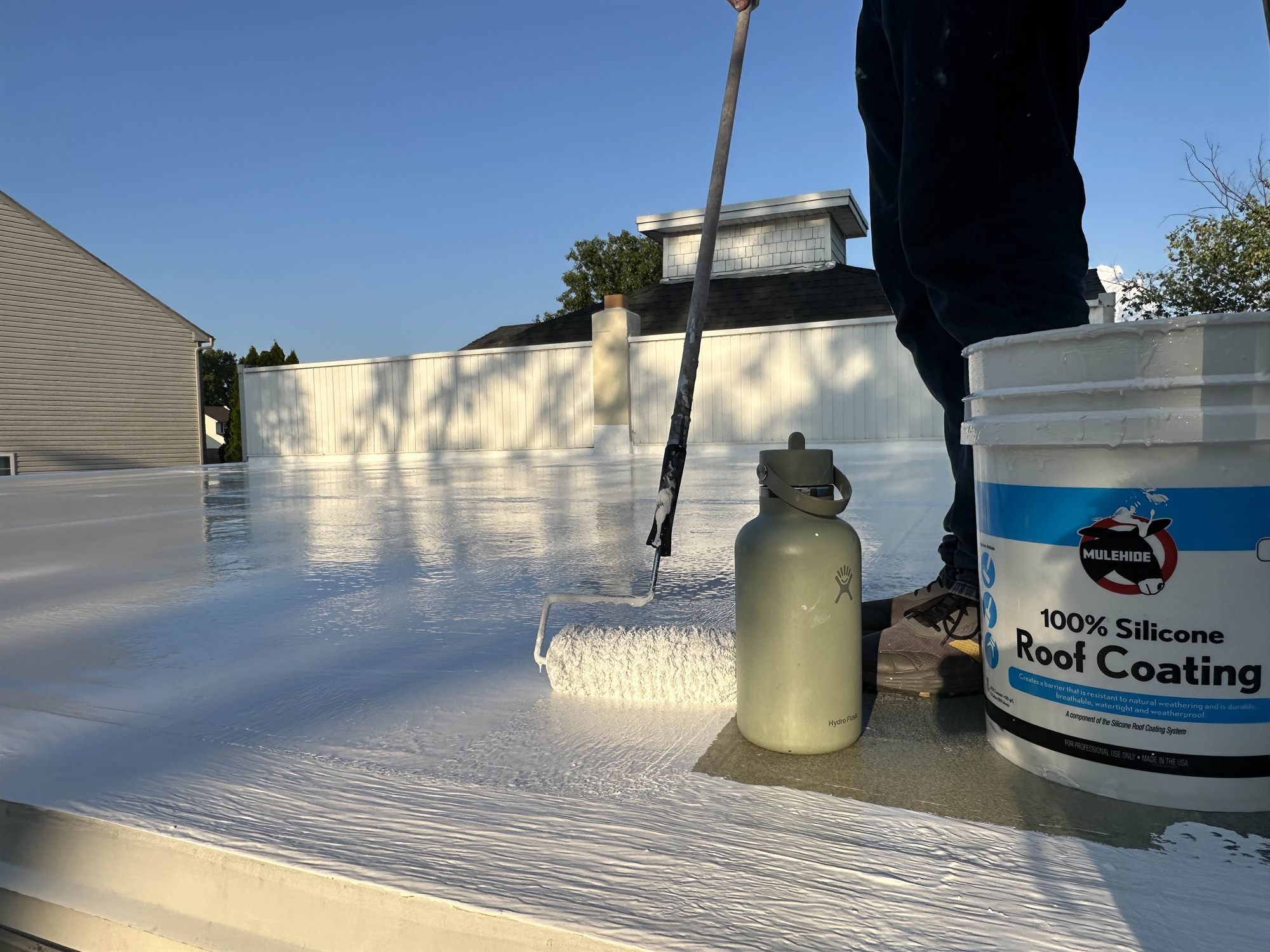 Roofer rolling Mule-Hide 100% silicone coating across a flat roof